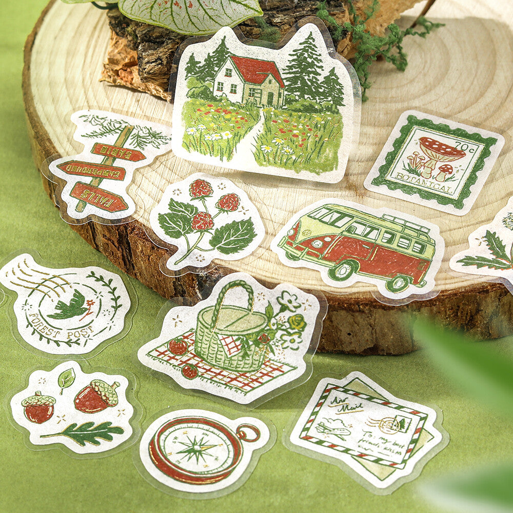 Close-up of BGM To the Forest foil-stamped flake stickers with cottage, hedgehog, picnic basket, compass and travel motifs